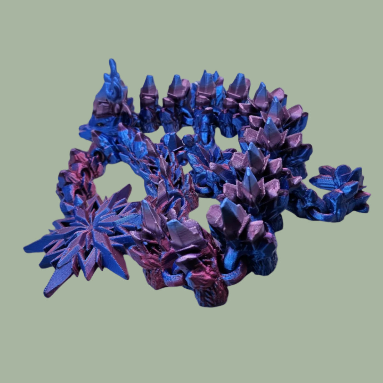 3D printed articulated dragon with snowflake details and large snowflake on tail, in a blue/purple/pink colour