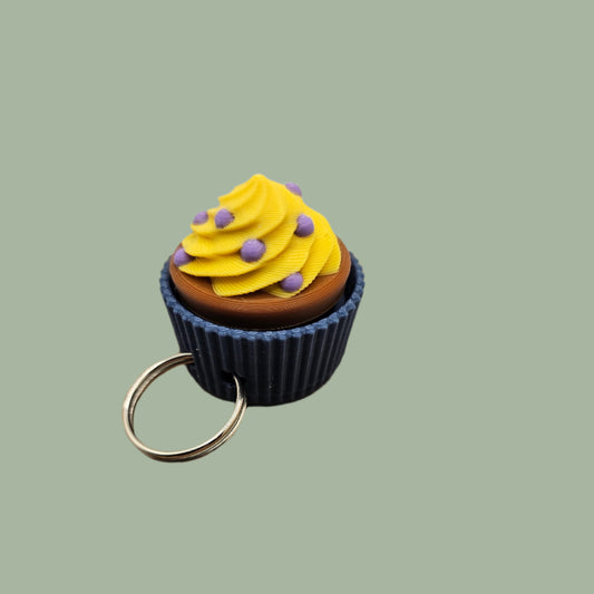 3D printed mini cupcake clicker keyring, with blue base, brown cake, yellow icing, and purple sprinkles