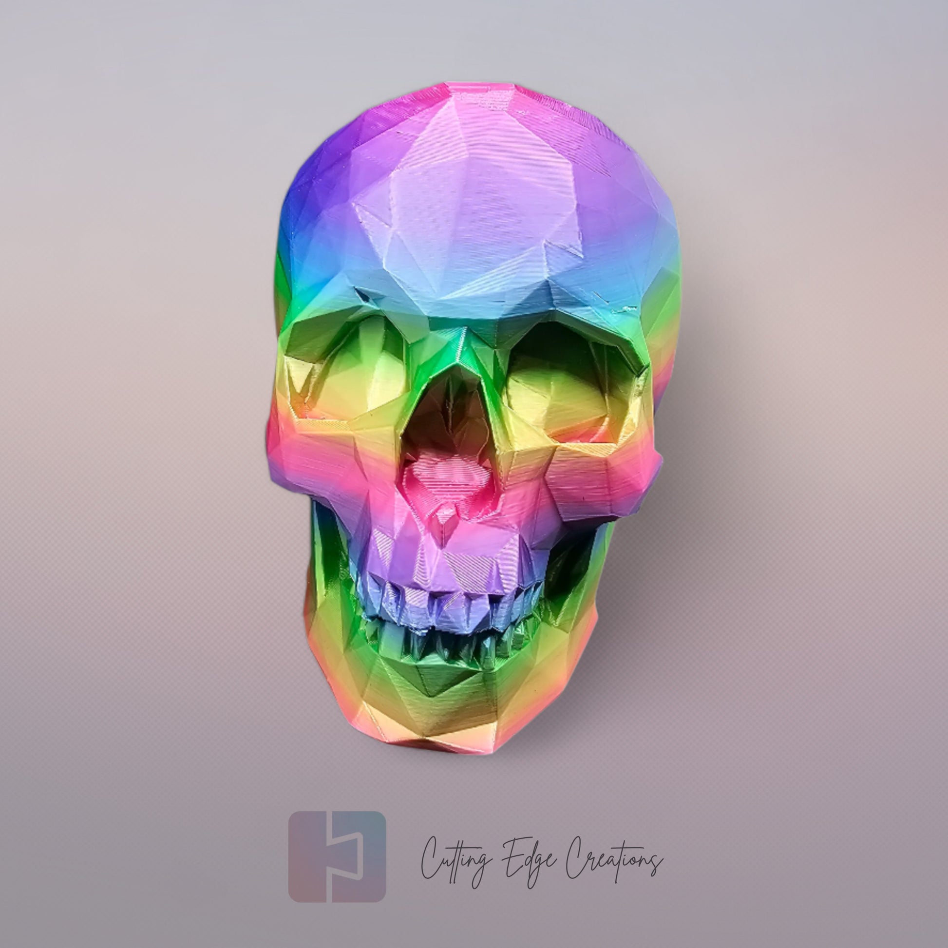 3D-printed low-poly rainbow skull figurine, uniquely coloured with a vibrant gradient. Handmade in the UK, 12cm tall, and perfect for modern home decor or gothic-inspired interiors
