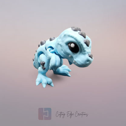 3D printed Love O’Saurus Rex dinosaur toy in light blue with black heart-shaped markings, designed as a flexible and posable fidget toy. Made in the UK by Cutting Edge Creations