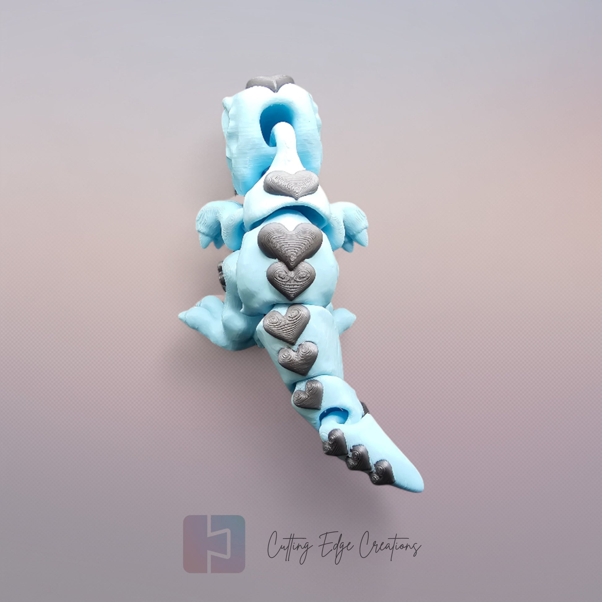 3D printed Love O’Saurus Rex dinosaur toy in light blue with black heart-shaped markings, designed as a flexible and posable fidget toy. Made in the UK by Cutting Edge Creations