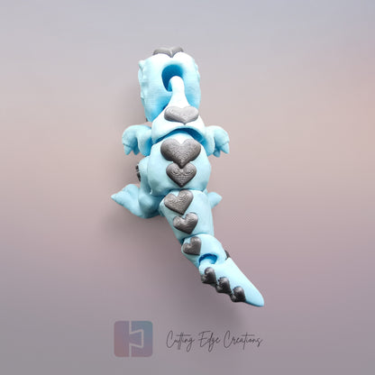 3D printed Love O’Saurus Rex dinosaur toy in light blue with black heart-shaped markings, designed as a flexible and posable fidget toy. Made in the UK by Cutting Edge Creations