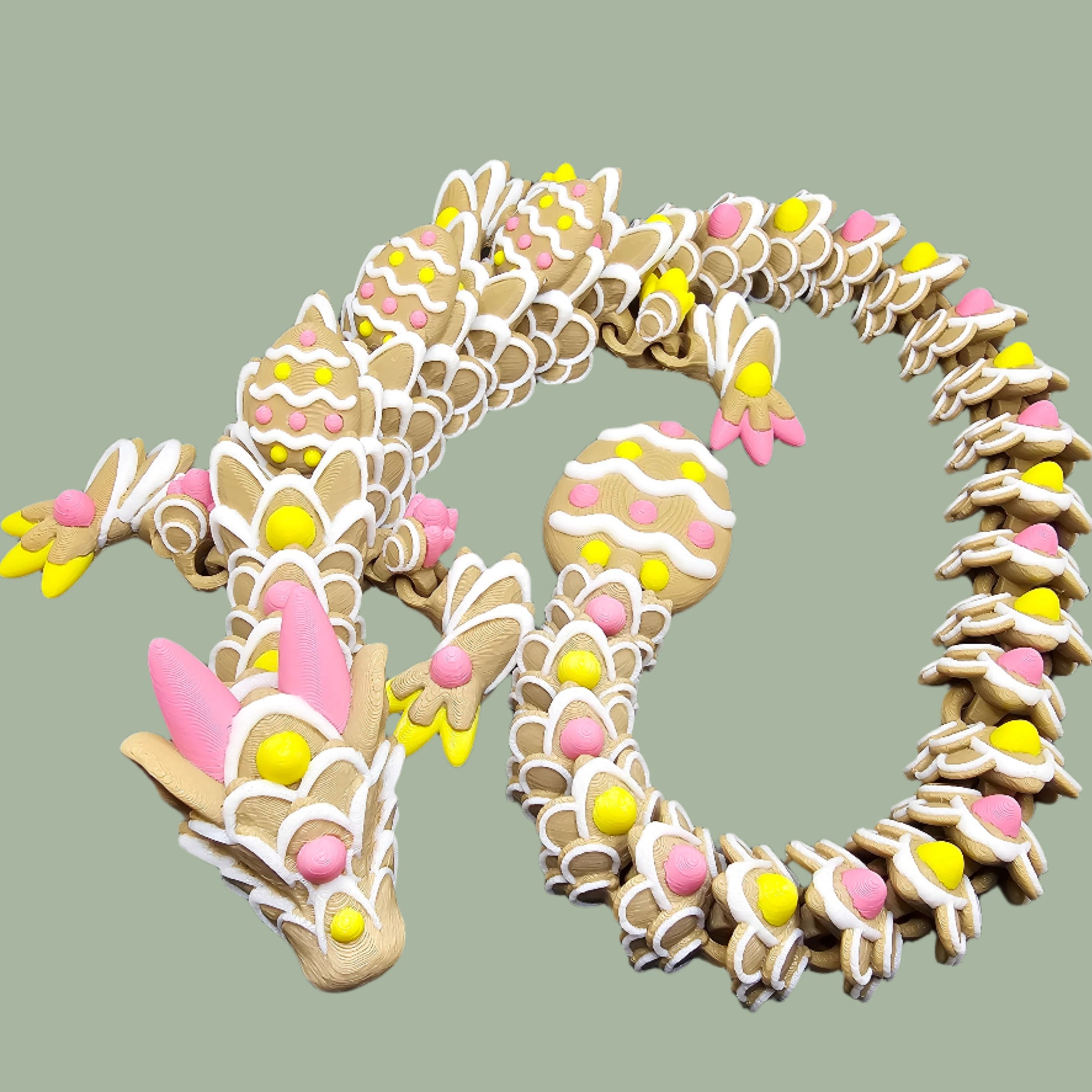 3D-printed Easter Cookie Dragon figurine, designed to resemble a decorated sugar cookie with pastel pink, yellow, and white icing details. Features Easter egg-shaped cookies along its body and tail. Handmade in the UK and available in Medium, Large, and X-Large sizes.