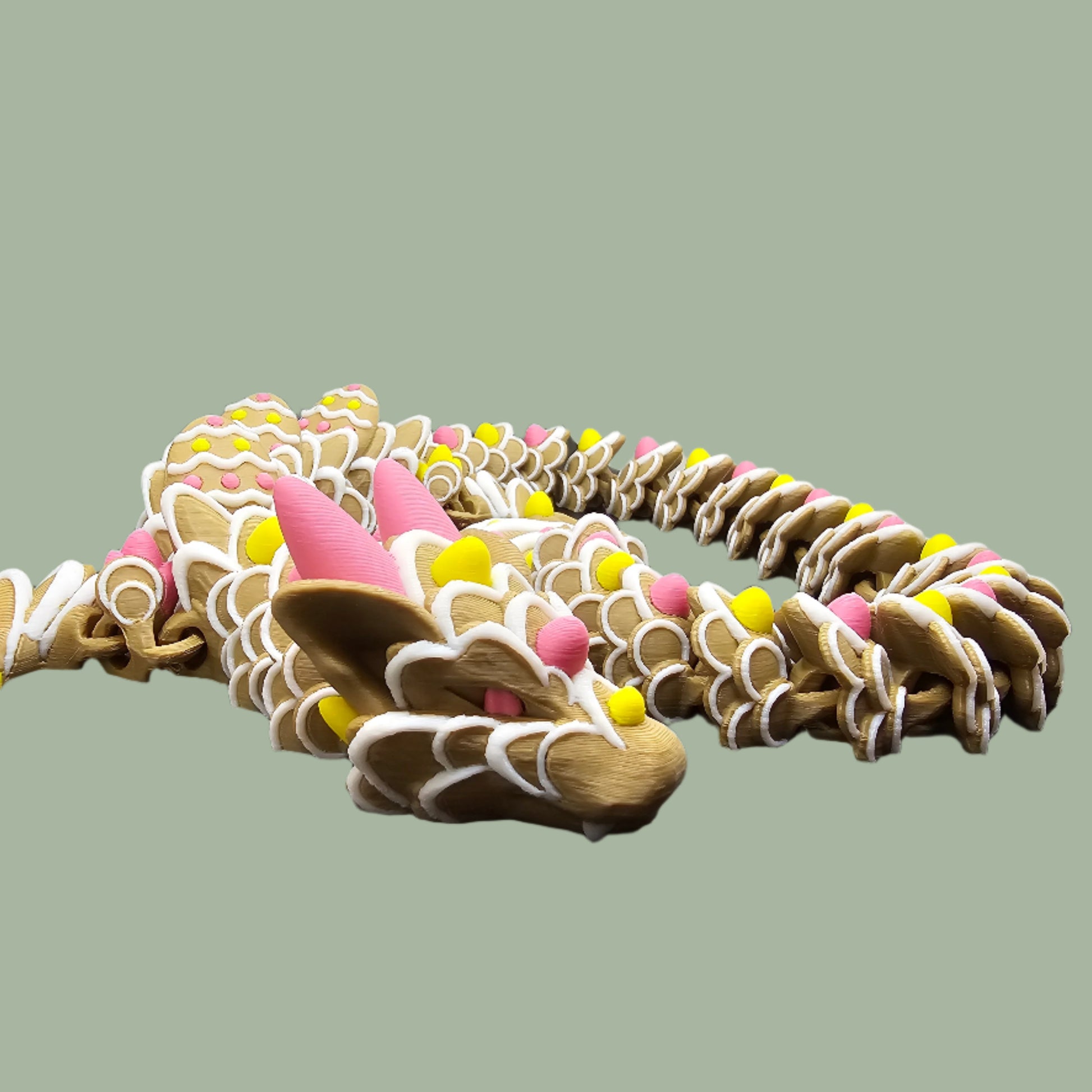 3D-printed Easter Cookie Dragon figurine, designed to resemble a decorated sugar cookie with pastel pink, yellow, and white icing details. Features Easter egg-shaped cookies along its body and tail. Handmade in the UK and available in Medium, Large, and X-Large sizes.
