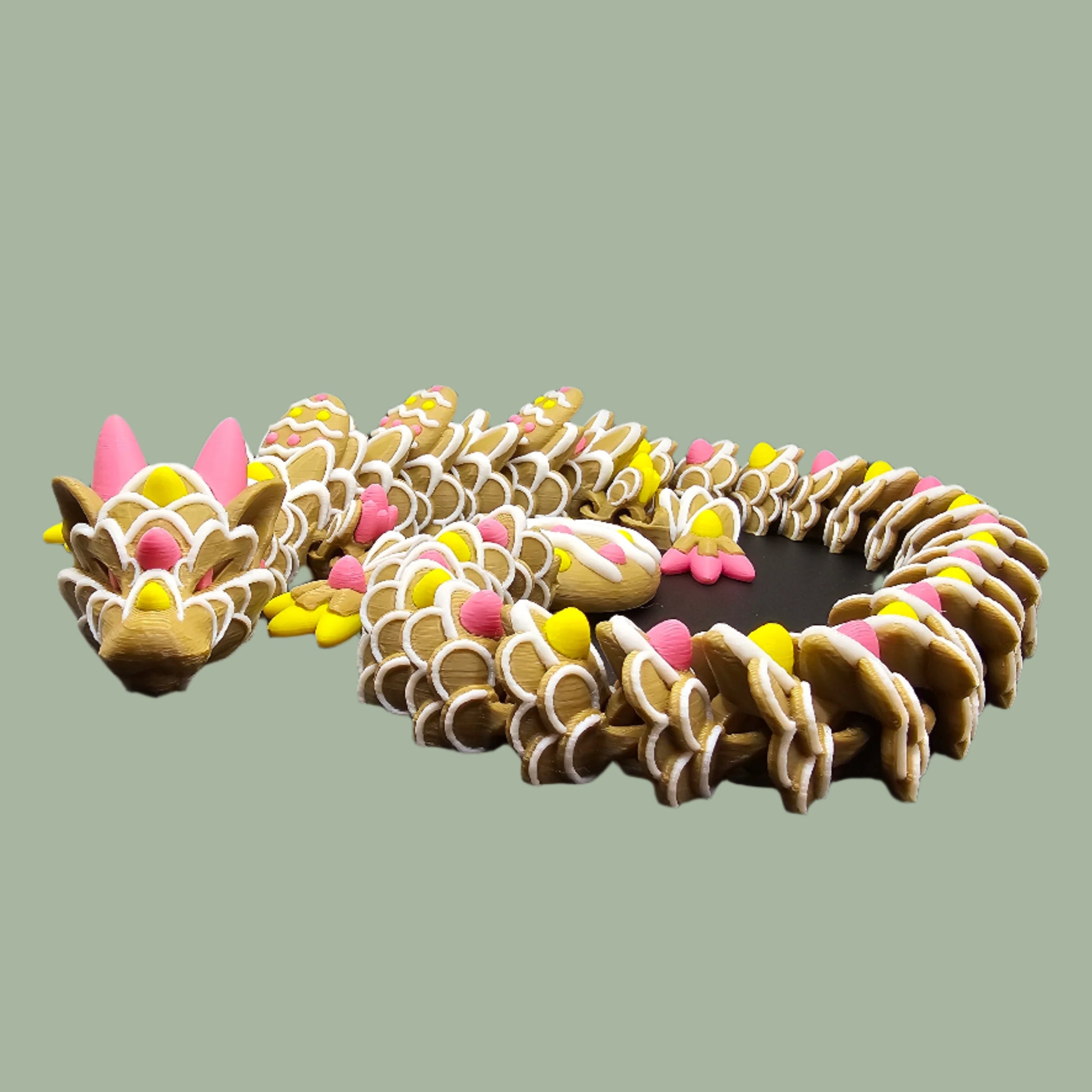 3D-printed Easter Cookie Dragon figurine, designed to resemble a decorated sugar cookie with pastel pink, yellow, and white icing details. Features Easter egg-shaped cookies along its body and tail. Handmade in the UK and available in Medium, Large, and X-Large sizes.