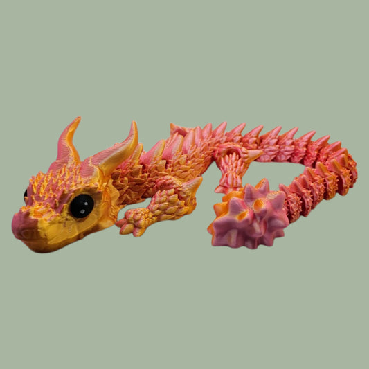 3D printed articulated dragon with large horns and spines along the body, in an orange/yellow colour