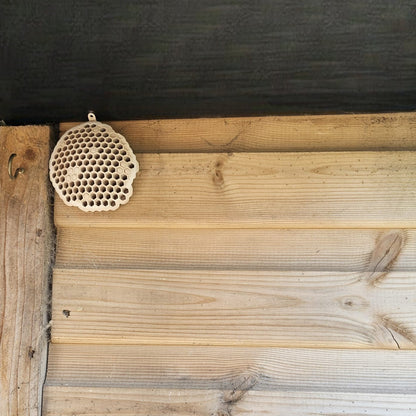 A 3D printed fake wasp nest with a honeycomb pattern, mounted under a wooden shed roof to deter real wasps.