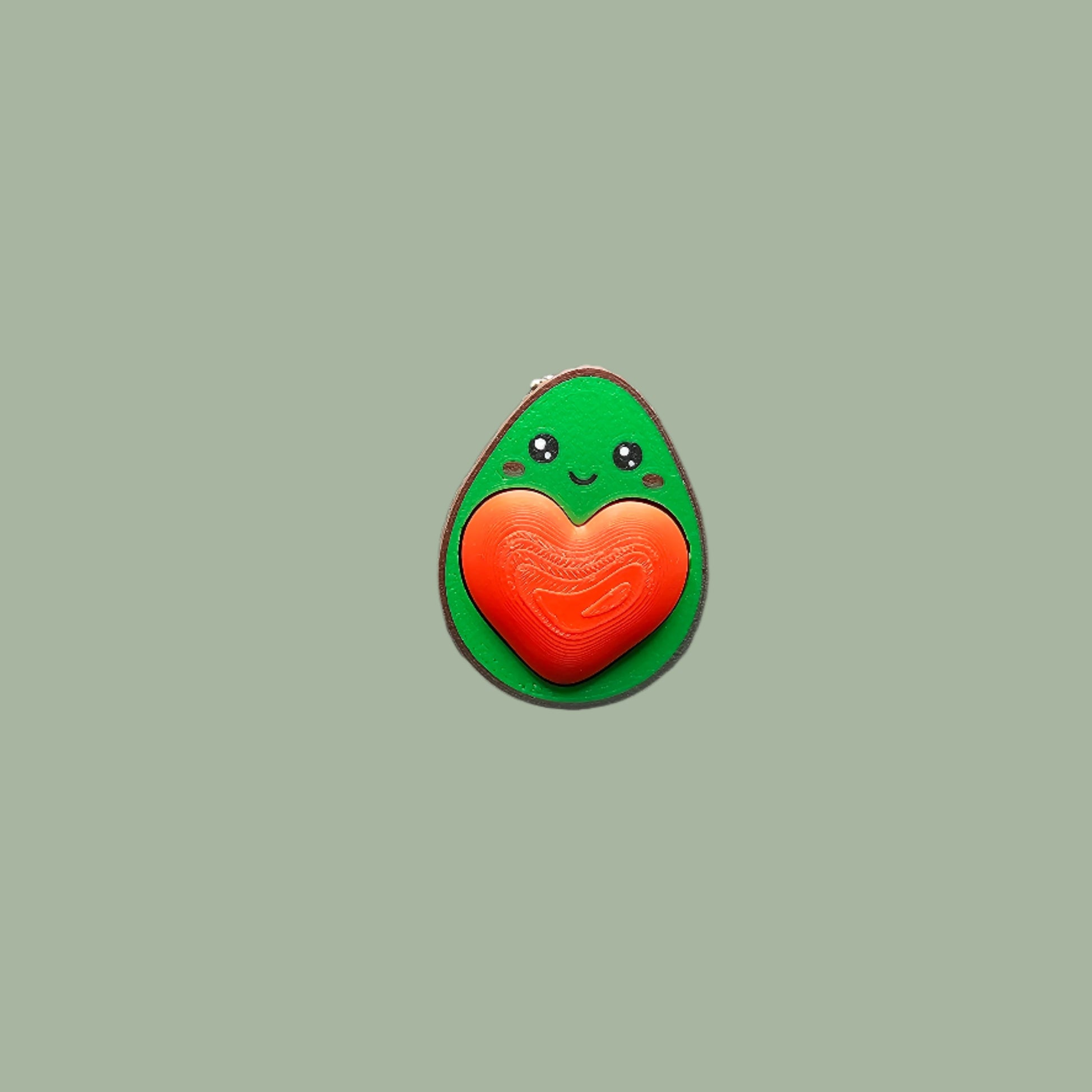 Cute 3D-printed avocado fidget clicker keychain with a heart-shaped clickable stone. Small stress relief toy, 5.5cm tall, made in the UK. Perfect for fidgeting, anxiety relief, and as a fun keyring accessory